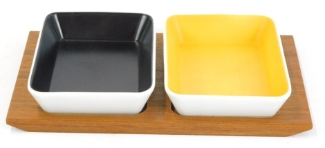 A continental serving tray, with two dishes, one with black and one with yellow interior, on a teak base, 4cm high, 22cm wide and 16cm deep.