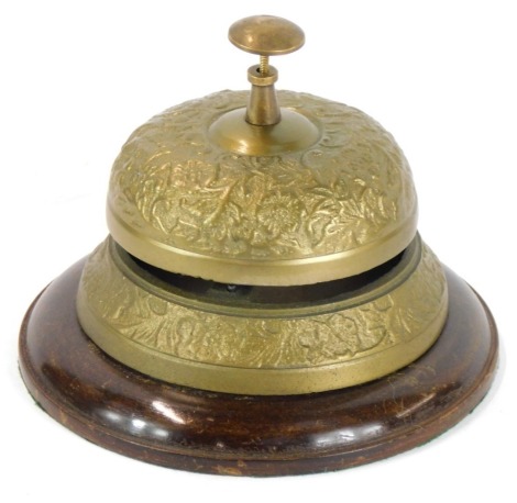 An early 20thC brass reception bell, over two tiers with floral vine supports, on a circular mahogany base, 13cm high, 4cm diameter.