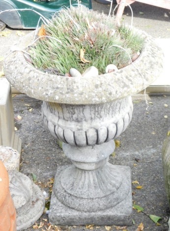 A reconstituted stone garden urn, the fluted top, on flared rim and square set base, 70cm high, 54cm diameter.