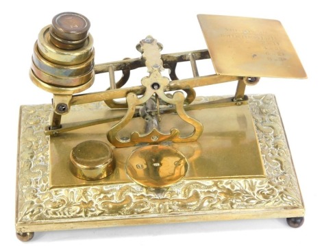 A brass postal scale set, on a rococo scroll base with bun feet and set of six weights, 14cm high, 20cm wide, 13cm deep