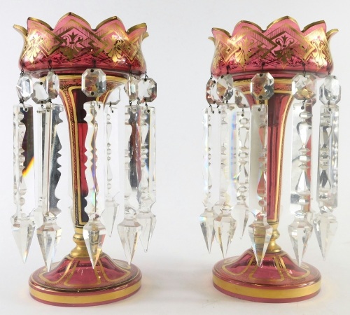 A pair of late 19thC Bohemian ruby glass lustres, with gilt highlights, floral tops, inverted stems and circular feet, with plain cut glass droppers, 29cm high. (2)