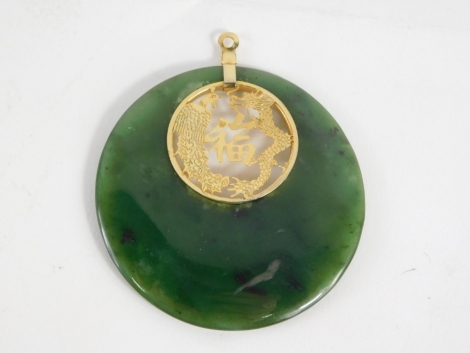 A jade coloured pendant, partially pierced with dragon and Chinese lettering, with yellow coloured metal mount, 6cm diameter.