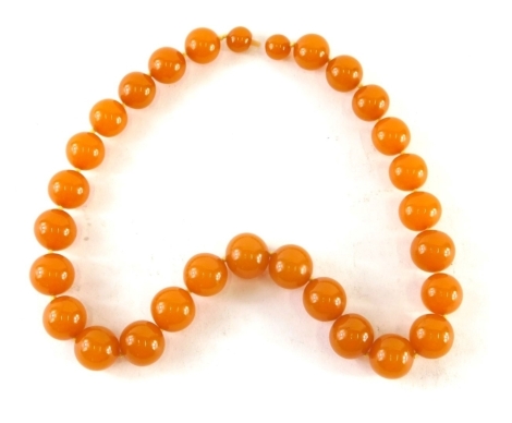 An orange amber bead necklace, with graduated beads on knotted string strand, the largest bead 2cm wide, the smallest 1.5cm wide, with screw in clasp, 53cm long, 91.3g all in.