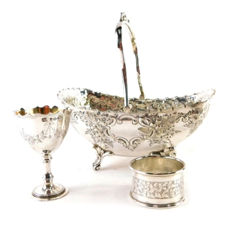 An Edwardian silver plated basket, with swing handle, repousse decorated floral and scroll body, and shaped feet, 17cm wide, a silver napkin ring and egg cup, 2.5oz of silver. (3)