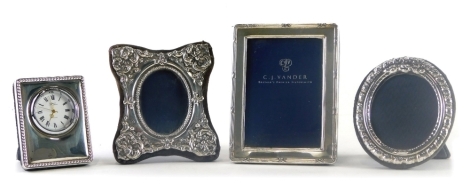 An Elizabeth II silver photograph frame, of rectangular form with a cross and line border and blue velvet easel back, London 1996, 11cm x 8cm, a further silver photograph frame repousse decorated, another, and an R Carr plated travel clock. (4)