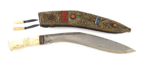 An Eastern kukri, with elaborate jewelled scabbard, set with turquoise and other paste, part decorated blade and turned bone handle with two bone handled knives, 45cm long.