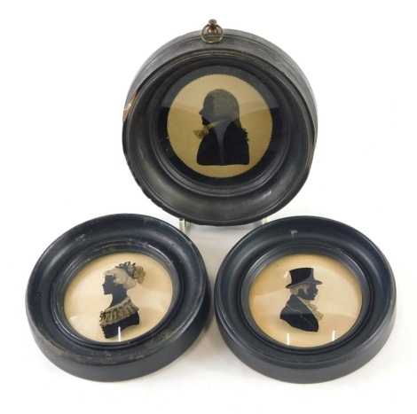 An early 20thC oval silhouette of a gentleman, quarter profile on glass, 8cm x 7cm, and two further circular silhouettes of a lady and gentleman. (3)