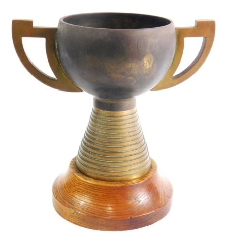 An unusual metal trophy, with angular handles, stepped circular tapering base and oak socle, the main body marked Presented by Major AGG Davidson, 19cm high.