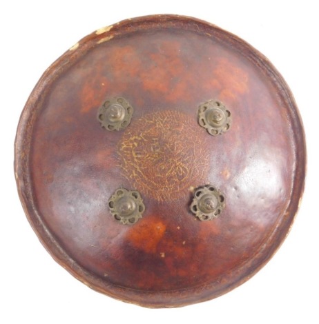 A 19thC Indian hide shield, of circular form, set with raised metal floral roundels, 34cm diameter.