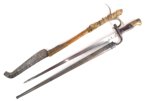 An early 20thC St Etienne bayonet and scabbard, with wooden handle and brass pommel with plain metal scabbard, marked to the side of the blade, 67cm long. and a further tribal edged weapon.