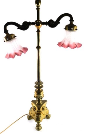 A 20thC two branch brass table lamp, with cylindrical reeded section and upper S scroll sections holding frosted pink, white and clear glass shades, on a tricorn base terminating in ball and claw feet, 82cm high.WARNING! This lot contains untested or unsa