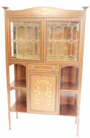 An Edwardian mahogany and marquetry Art Nouveau display cabinet, in the manner of Shapland and Petter, the shaped top with tapering finials, above two glazed doors, each with gilt leaded glass enclosing a velvet lined interior, above an arrangement of one