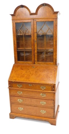 A burr elm bureau bookcase in Queen Anne style, with a doubled domed top above two astragal glazed doors enclosing shaped shelves, the fall enclosing a fitted interior above four graduated drawers each with pierced brass handles on bracket feet, 199cm hig