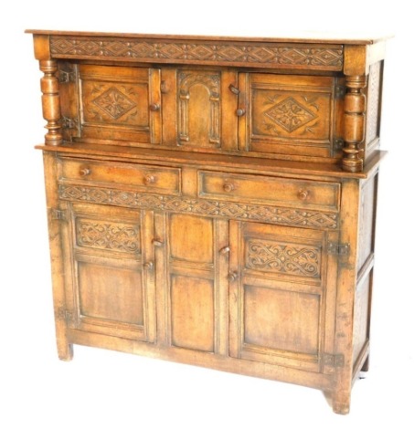 An oak court cupboard in 17thC style, with a carved frieze, on turned supports with two panelled doors, the base with a further two drawers and two panelled doors on styles, with butterfly shaped iron hinges, 135cm high, 130cm wide.