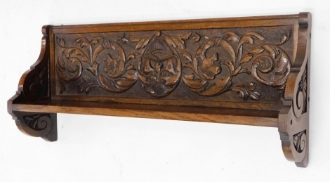 An early 20thC carved oak wall shelf, mounted with scrolls, masks etc, and with shaped end supports. 76cm wide