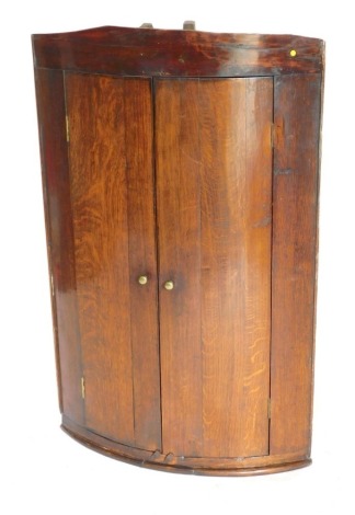 A 19thC oak and mahogany bowfront hanging corner cupboard, with turned brass handles, 94cm high, 59cm wide.