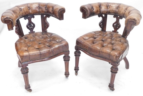 A pair of Victorian mahogany library chairs, upholstered in buttoned leather, with carved shaped back, on turned legs with castors.