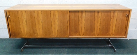 An Indian rosewood and chrome plated sideboard, designed by Richard Young for Merrow Associates, with sliding doors enclosing glass shelves and drawers, on chrome plated end supports, 77cm high, 184cm wide, 45cm deep.