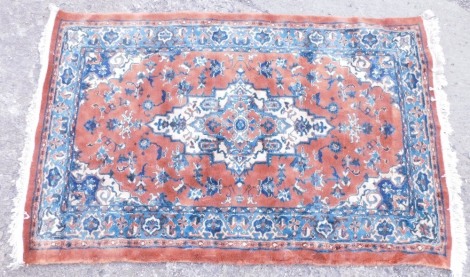 A Belgium cotton machine woven rug, in the Persian style with a design of flowers, etc., on a orange ground with blue spandrels, 181cm x 116cm.