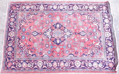 A Persian rug, with a central medallion surrounded by flowers, leaves, etc., on a pink/red ground, with spandrels, one wide and two narrow borders.