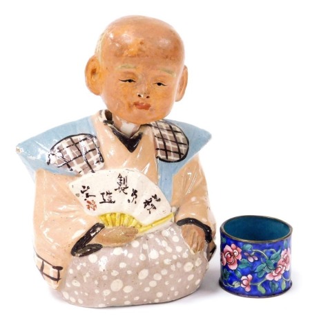 An early 20thC Japanese pottery nodding figure, modelled as a seated sage holding a fan, bears script, 15cm high, together with a Chinese brass and enamel napkin ring. (2)