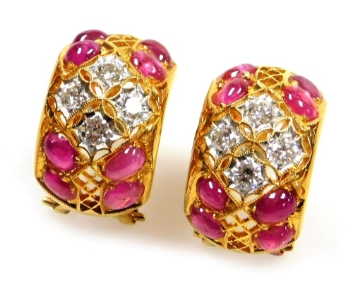 A pair of cabachon ruby and diamond set open work earrings, each set with eight rubies of 3.5mm x 2.5mm, with a central diamond set motif, each of four diamonds of 2.5mm diameter approx, in precious yellow metal clip and pin backs, 10.4g all in.