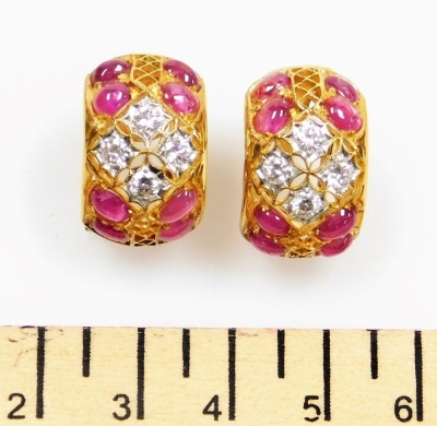 A pair of cabachon ruby and diamond set open work earrings, each set with eight rubies of 3.5mm x 2.5mm, with a central diamond set motif, each of four diamonds of 2.5mm diameter approx, in precious yellow metal clip and pin backs, 10.4g all in. - 2