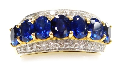 A sapphire and diamond set dress ring, a central row of sapphires of 5mm x 3.5mm average faceted stones, seven total of various hue and saturation, flanked by rows of tiny diamonds, all set in precious yellow metal, size P, 7.3g all in.