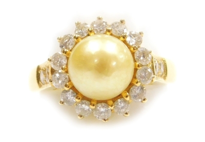 A pearl and diamond set dress ring, a 7.3mm diameter cultured pearl, pinned and glued centrally, yellow tinge, surrounded by tiny diamonds to each shoulder, set in precious yellow metal, 4.7g all in, size K.