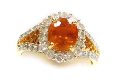 A padparadsha sapphire and diamond set dress ring, the central stone of 7.09mm x 6.3mm, facet cut, golden hue with a pink tinge, surrounded by tiny diamonds and diamond set pierced shoulders, all in precious yellow metal, size L, 5.7g all in.