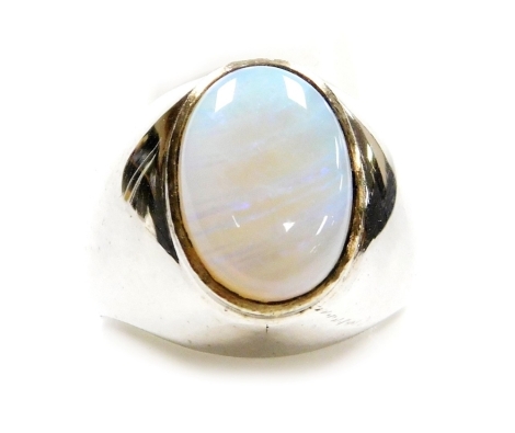 An opal set dress ring, the flat cabachon opal of 13.6mm x 9.7mm showing flashes of green, blue and purple, set in a white metal chunky mount, size R, 9.5g all in.