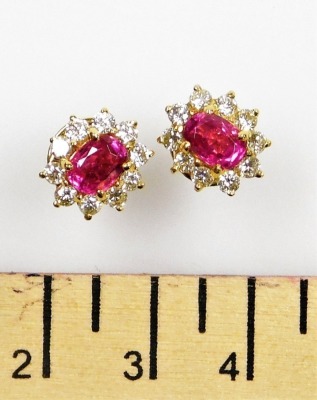 A pair of ruby and diamond cluster earrings, the central facet cut ruby of 6.1mm x 5.2mm surrounded by ten round brilliant cut diamonds of 1.5mm diameter average, post and butterfly backs, set in precious yellow metal, 5.1g all in. - 2