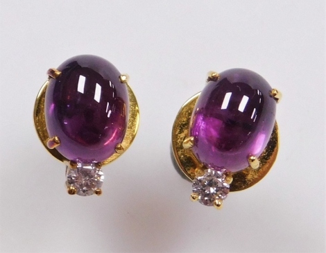 A pair of oval cabachon ruby and diamond stud earrings, the purple hue ruby of .4mm x 5.8mm approx topped by a round brilliant cut diamond of 2mm diameter, each stud 1cm x 0.6cm, set in precious yellow metal, 4.5g all in.