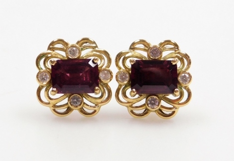 A pair of tourmaline and diamond ornate earrings, the rectangular faceted stone of 8mm x 5.9mm with tiny diamonds to the cardinal points, with scrollwork surround, 1.2cm x 1.1cm each, to post and butterfly back, 6.3g all in.