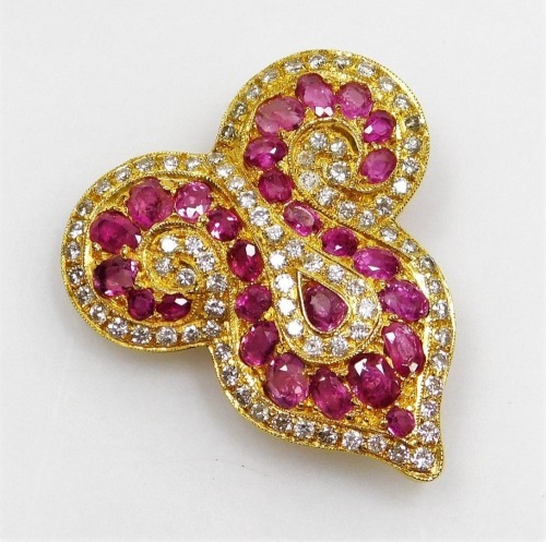 A ruby and diamond set brooch, of Eastern scroll shape set with twenty seven oval faceted rubies ranging in size from 1.3mm to 3mm long approx, with a tiny diamond set complete surround, the whole in precious yellow metal, pin back, 2.8cm x 107cm, 10.6g a