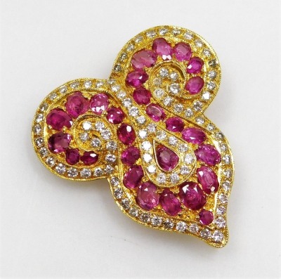 A ruby and diamond set brooch, of Eastern scroll shape set with twenty seven oval faceted rubies ranging in size from 1.3mm to 3mm long approx, with a tiny diamond set complete surround, the whole in precious yellow metal, pin back, 2.8cm x 107cm, 10.6g a