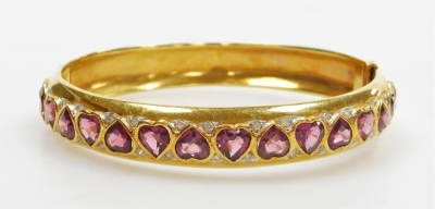 A ruby and diamond set hinged bangle, the front set with sixteen heart shaped facet cut rubies, inset both sides with tiny diamonds, rubies 4.5mm x 5.6mm approx average, internal diameter 5.4cm, external diameter 6cm, 34.5g all in.