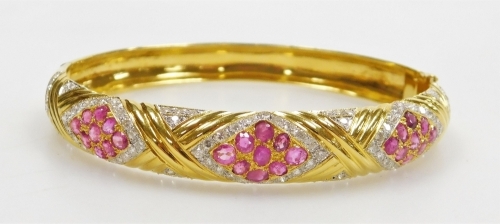 A ruby and diamond set hinged bangle, three ruby set lozenge shaped motifs of nine stones of 2mm each, surrounded by tiny diamonds with cross over raised pattern between, internal diameter 6cm, external diameter 6.5cm, 27.9g all in.