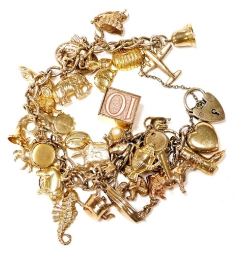 Withdrawn pre sale - A 9ct gold charm bracelet, with thirty one charms as fitted, on a heart shaped padlock clasp, with safety chain, 50.4g.