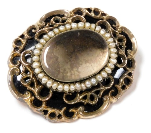 A Victorian hair locket mourning brooch, of oval form, with black enamel and yellow metal, the glass fascia border by seed pearls, engraved verso 'In Memory of Thomas Campbell, Ouston Grange, Died Oct 2 1872'.