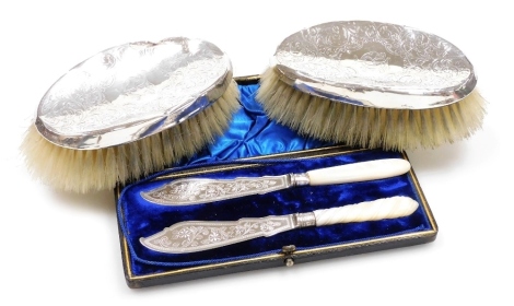 A pair of George V silver mounted clothes brushes, each with bright cut decoration and initialled, Chester 1912, and a pair of Victorian butter knives with silver blades and mother of pearls handles, Sheffield 1891, in fitted box.