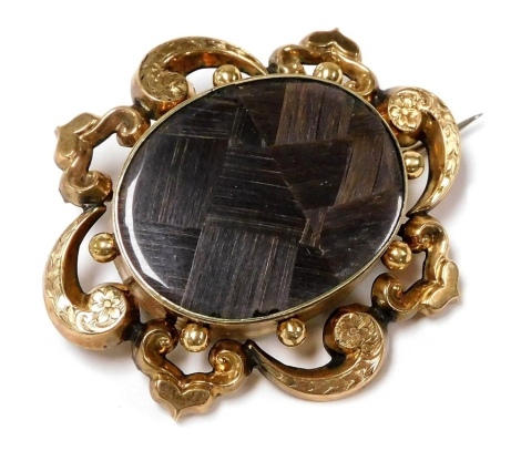 A Victorian hair locket mourning brooch, set in yellow metal, in an engraved foliate and heart scroll surround, 5cm wide, 13.0g.