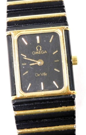 An Omega DeVille lady's gold plated and black metal wristwatch, rectangular black dial bearing batons, on a bracelet strap.