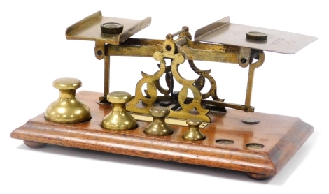 A set of early 20thC brass postal scales, with weights, on a wooden base, 24cm wide.