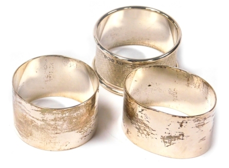 A silver napkin ring, with engine turned decoration, Sheffield 1963, and two further napkin rings, one oval the other circular, of plain form, Sheffield 1975, 2.95oz.