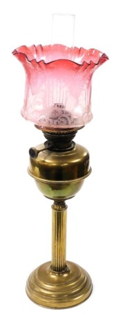 An early 20thC brass oil lamp, with a graduated pink glass shade, with etched floral decoration chimney, brass reservoir on a Corinthian column and stepped base, 70cm high.