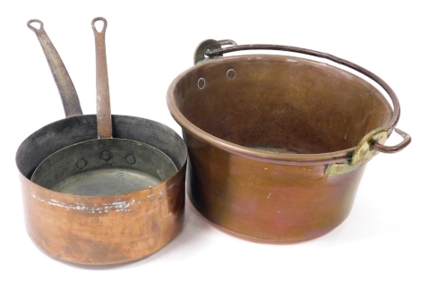 A copper jam pan, with a cast iron handle, 35cm wide, and a pair of graduated copper saucepans. (3)