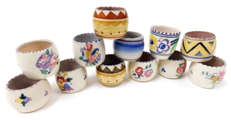 Twelve Poole pottery egg cups, traditionally painted with flowers, or with geometric banding, impressed marks.