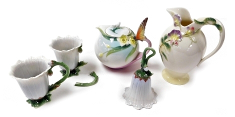 A Franz porcelain teapot, moulded with flowers with a butterfly handle, XP1878, a jug moulded with flowers FZ00411, floral shaped bell FZ01275, and two mugs, FZ01045. (5, AF)