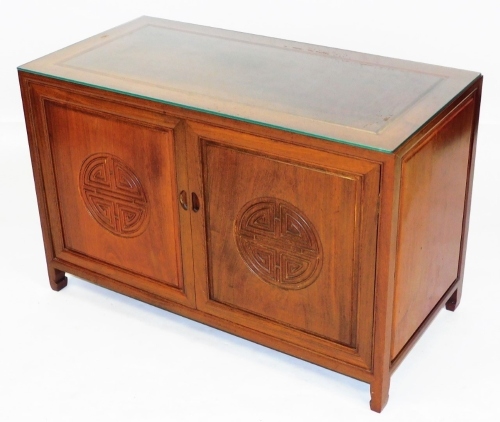 A Chinese hardwood cupboard, the top with a glass protector, with two carved doors opening to reveal a shelf and three recesses flanked to the right by three drawers, raised on square feet, 63cm high, 97cm wide, 48cm deep.